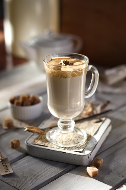 A glass of coffee with a spoon on a table next to it.