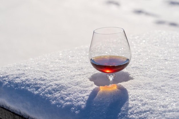 Glass of cognac on a bed of snow and white background close up