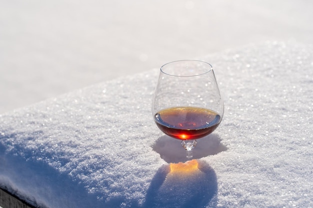 Glass of cognac on a bed of snow and white background close up