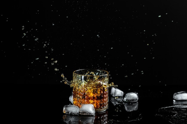 The glass of cognac or brandy isolated on a black background alcohol cocktail ice cubes fall into a glass with whiskey