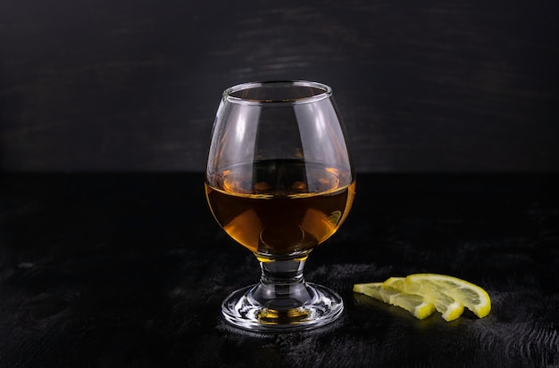 Glass of cognac with lemon  on a dark wooden background