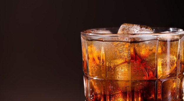 A glass of cola drink with ice cubes Fresh cold sweet cola drink with ice on brown background with copy space