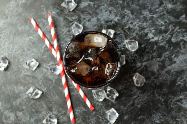 Glass of cola, ice and straws on black smokey background.