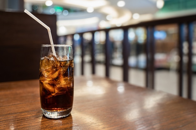 A glass of cola with ice cube on wooden table over blurred  restaurant background