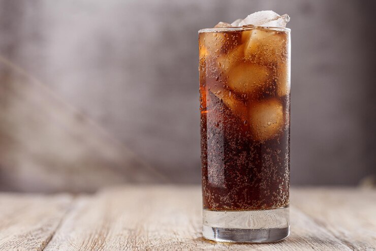 A glass of cola with ice on a wooden table