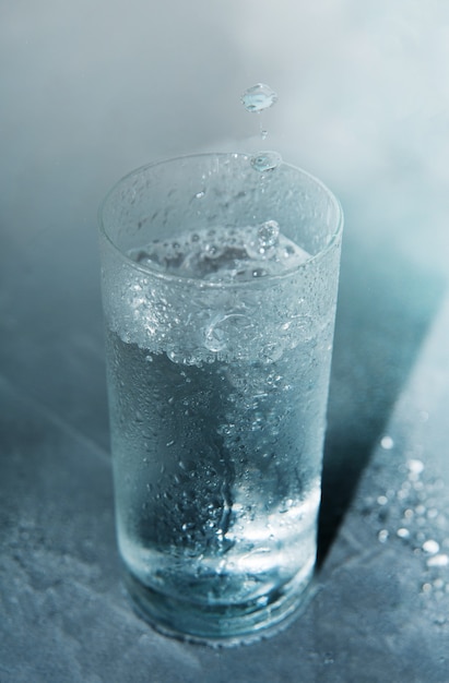 Photo glass of cold clear water on a blue background with falling drops into a glass.