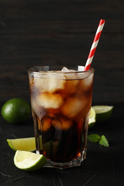 Glass of cold cola and limes on black cement background