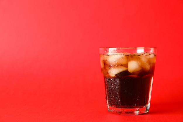 Glass of cold cola on red background, space for text