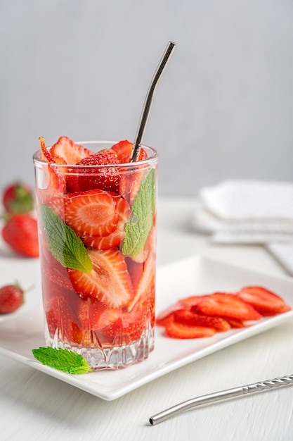 Glass of cold detox infused water drink made of sliced strawberries and mint leaves served on table