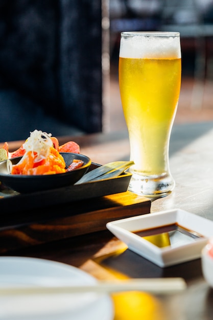 A glass of cold draft beer with froth on wooden table with blur meal in foreground