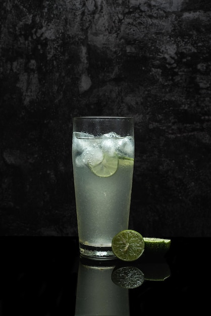 Glass of cold lemonade on black table. Ice cold drink on dark background.