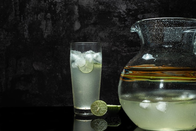 Glass of cold lemonade on black table. Ice cold drink on dark background.