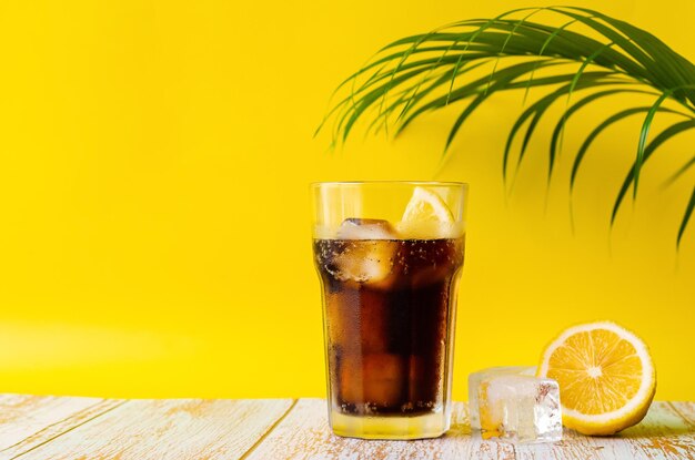 A glass of cold soft drink with lemon on wooden floor with coconut leaf summer drink concept