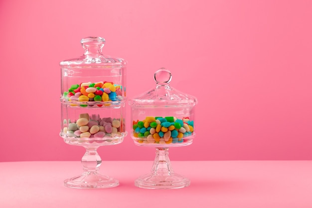 Photo glass containers with candies against pink background