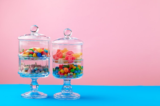 Glass containers with candies and sweets against pink
