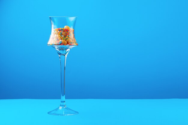 Glass containers with colorful candies against blue background close up