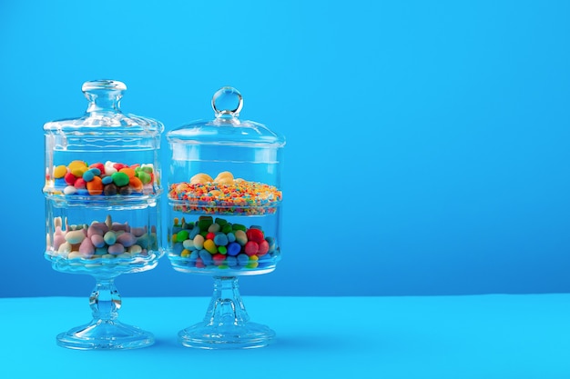 Glass containers with colorful candies against blue background close up