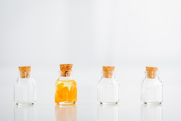 Glass corked jar with essential oil with orange slices near empty jars on white background