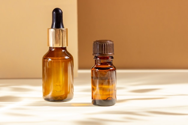 Glass cosmetic bottles with a dropper on a beige background with bright sunlight and hard shadows.