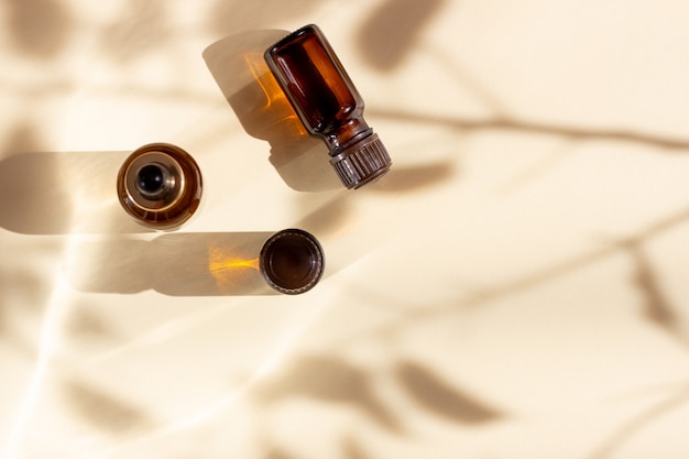 Glass cosmetic bottles with a dropper stand on a beige background with bright sunlight and shadows. The concept of natural cosmetics, natural essential oil.