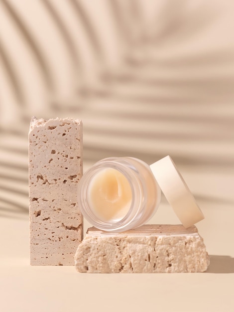 Glass Cosmetic jar on travertine stones on light beige close up palm leaf hard shadows