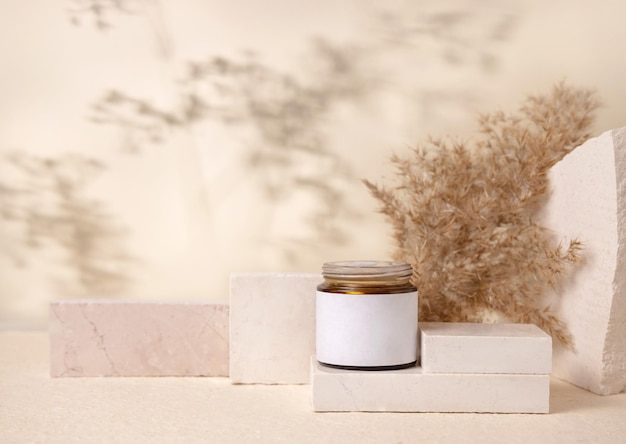 Glass cosmetic jar with blank label on stones near pampas grass close up Mockup