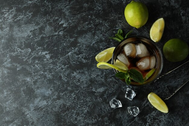 Glass of Cuba Libre and ingredients on black smokey surface