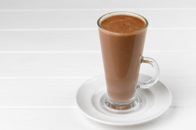 Стеклянная чашка напитка какао на белом деревянном столе крупным планом