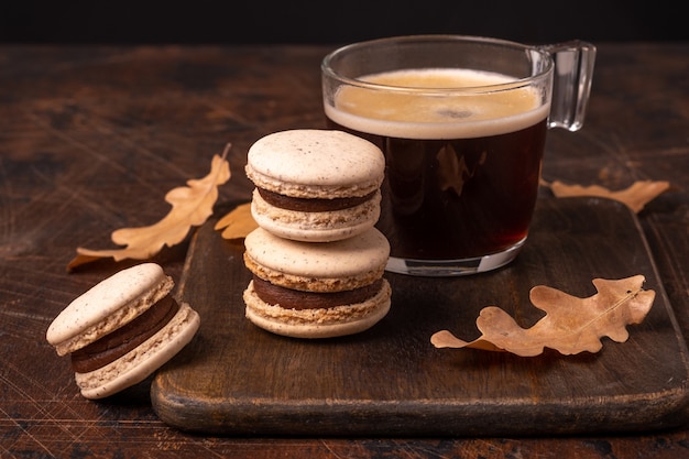 Glass cup of coffee and chocolate macarons on wooden background. Cozy autumn composition - Image