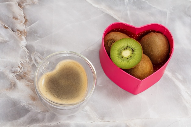 glass cup of coffee and a gift box with kiwi fruits on the kitchen table. the cup