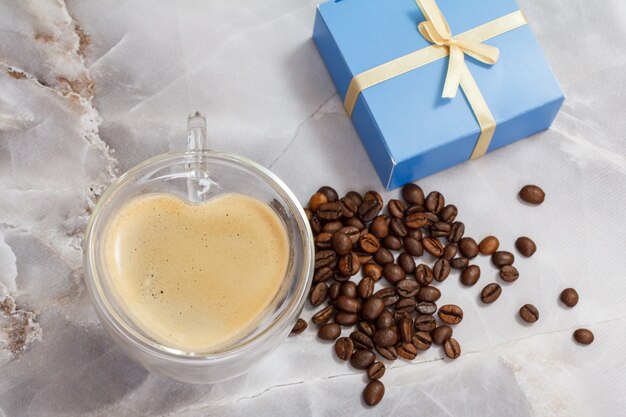 стеклянная чашка кофе в форме сердца, жареные кофейные зерна и подарочная коробка на кухонном столе.