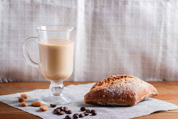 Glass cup of coffee with cream and bun