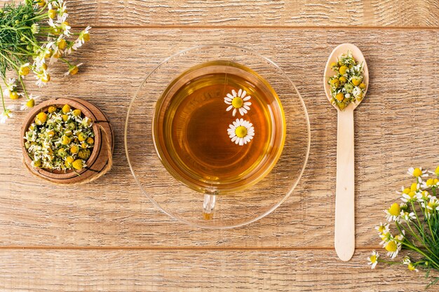 Tazza di vetro di tè verde con fiori di camomilla bianca e piccola botte di legno con fiori secchi di camomilla su tavole. vista dall'alto