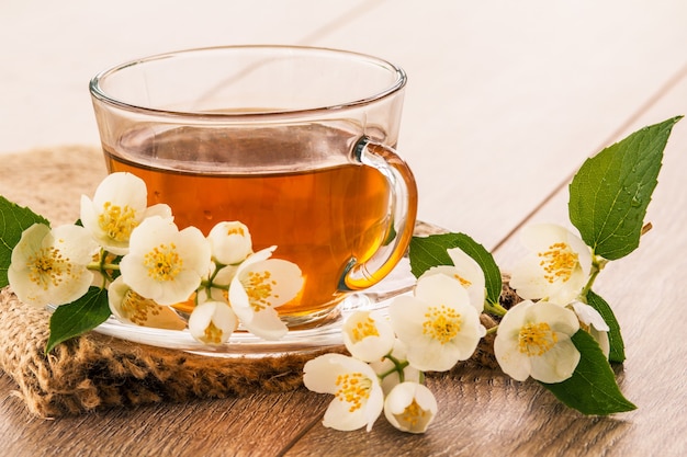 Glass cup of green tea with white jasmine flowers on wooden background