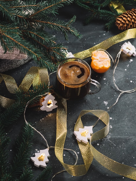 테이블에 뜨거운 에스프레소 커피 한 잔, 크리스마스 트리 형태의 화환, 가지. 가정적인 분위기와 편안함