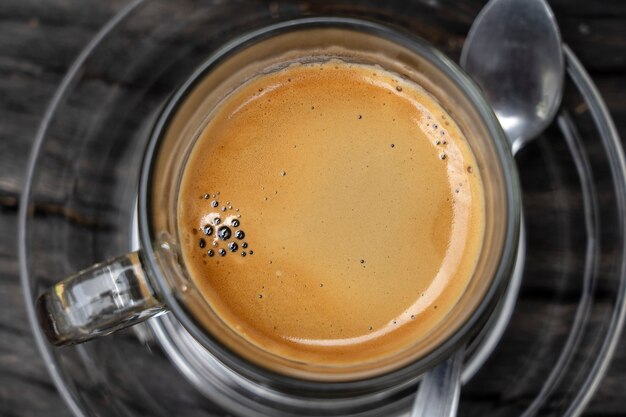 Стеклянная чашка горячего кофе эспрессо на деревянной доске, крупным планом, вид сверху