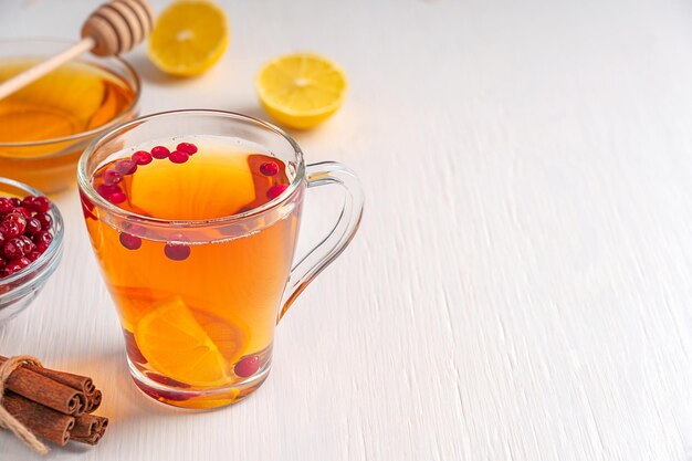 Glass cup of hot organic natural herbal tea with berries, lemon slices and honey on white table