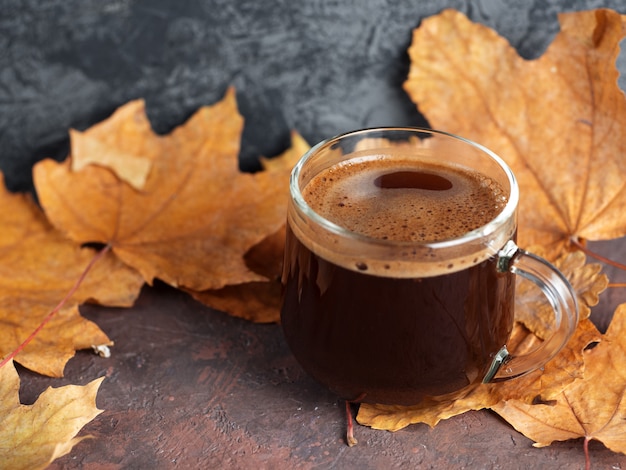 Фото Стеклянная чашка кофе в осенние листья. домашний уют по утрам