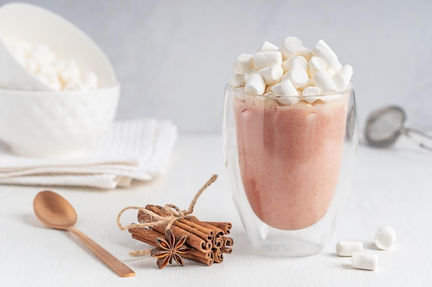 Foto coppa di vetro di bevanda al cacao dolce con topping di marshmallow su un tavolo di legno bianco con cannella di anice