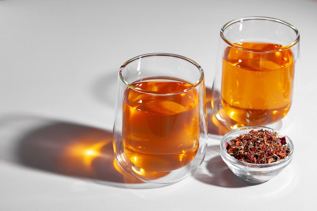 Glass cup of tea and dry tea leaves on white table