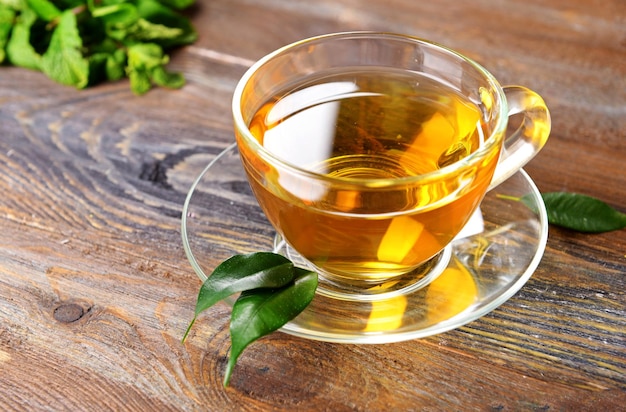 Glass cup of tea with green leaves on wooden background