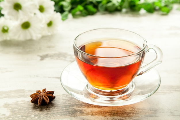 Glass cup of tea on a wooden table with flowers, mint leaves and star anise.