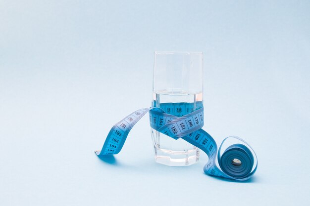 A glass cup of water wrapped in blue measuring tape