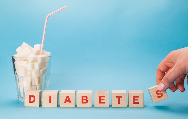 Фото Стеклянная чашка с соломой, полной кубов белого сахара. печатные буквы диабета в кроссворде.