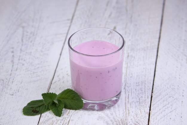 Tazza di vetro con yogurt ai mirtilli e menta su un tavolo in legno chiaro. sana colazione in una bella mattina