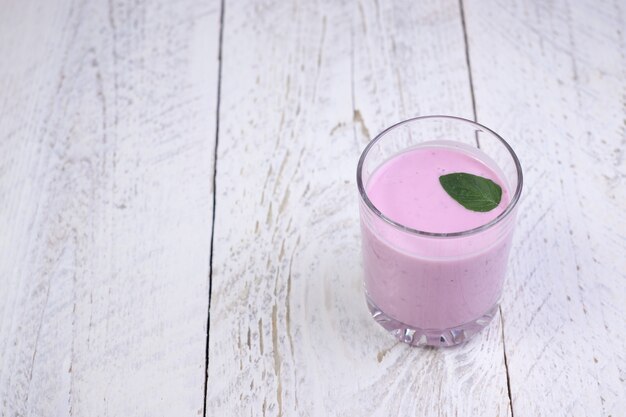 Glass cup with blueberry yogurt and mint on a light wooden table. Healthy breakfast on a fine morning