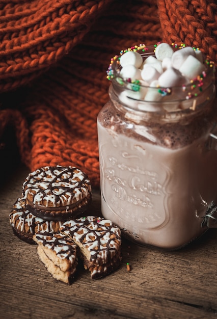 Glass Cup with cocoa and marshmallows, chocolate chip cookies and orange scarf