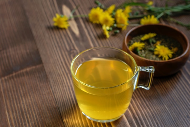 タンポポの花茶とガラスのカップ。茶道に備えて、木製のテーブルに乾いた茶葉と新鮮なタンポポの花を。