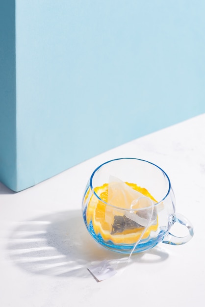 Tazza di vetro con la bustina di tè della frutta e la fetta di limone su una tavola bianca