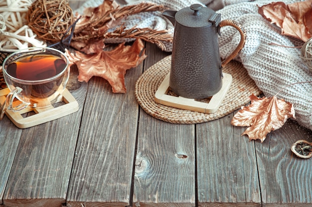 Glass cup with tea and teapot on wooden table with autumn decor details copy space.